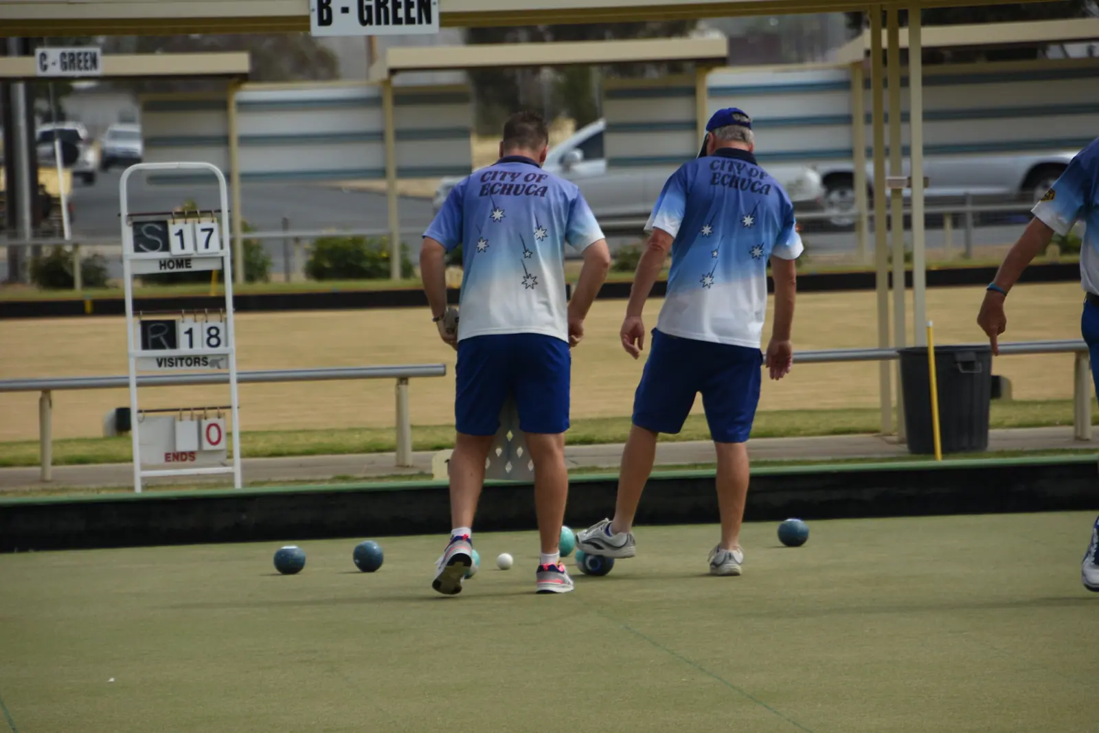 Two bowlers walking the rink as spectators watch from the shade