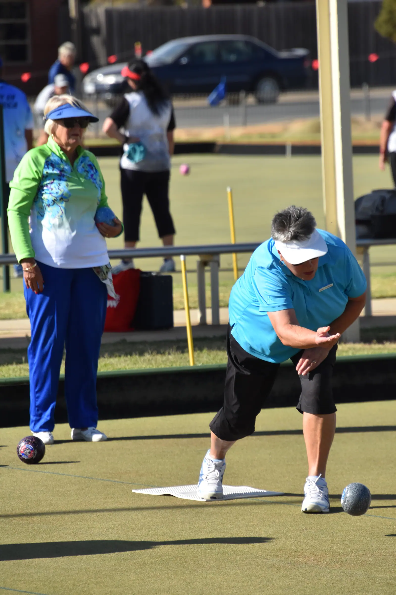 A player releasing a bowl down the rink on a bright tournament day